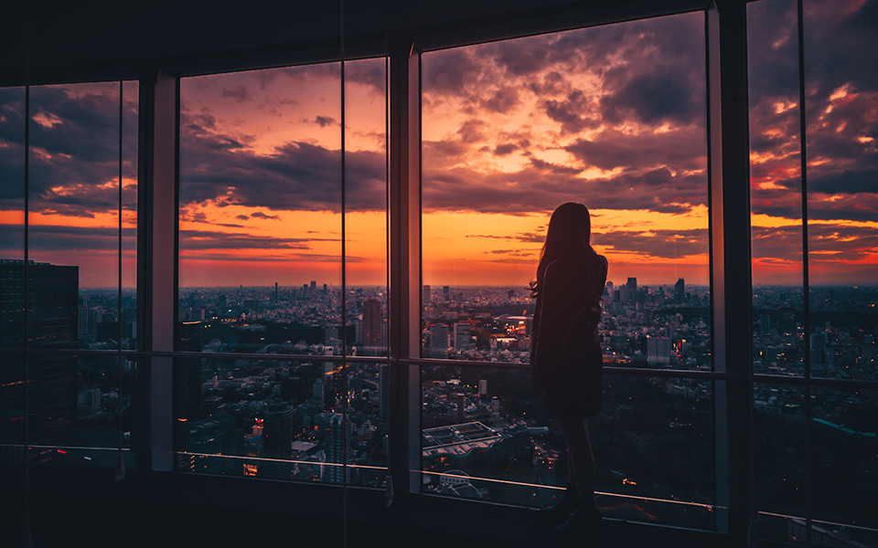 Frau in Wolkenkratzer blickt auf Stadt bei Sonnenuntergang
